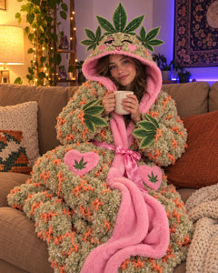Woman curled up on a couch in the Wake & Cozy robe, hood up, holding a mug